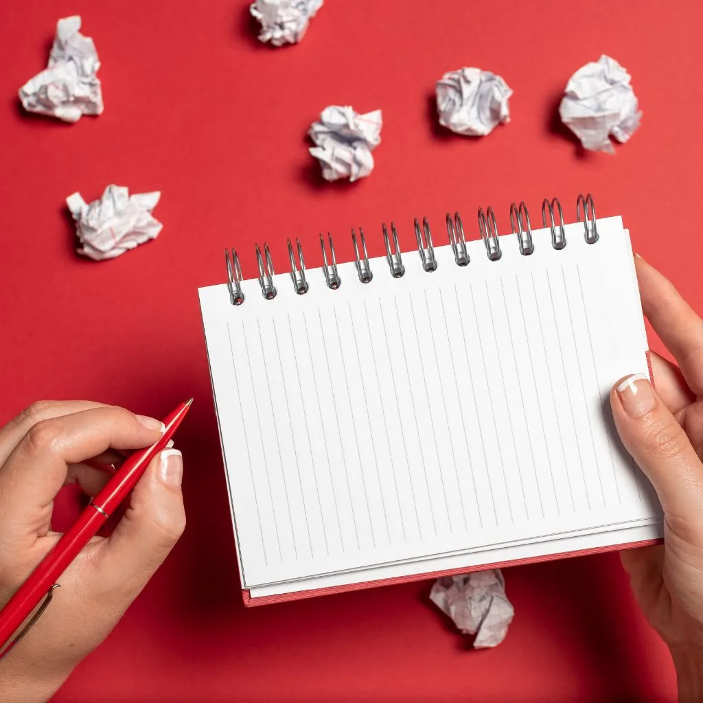 Handen met een leeg notitieblok omringd door proppen papier