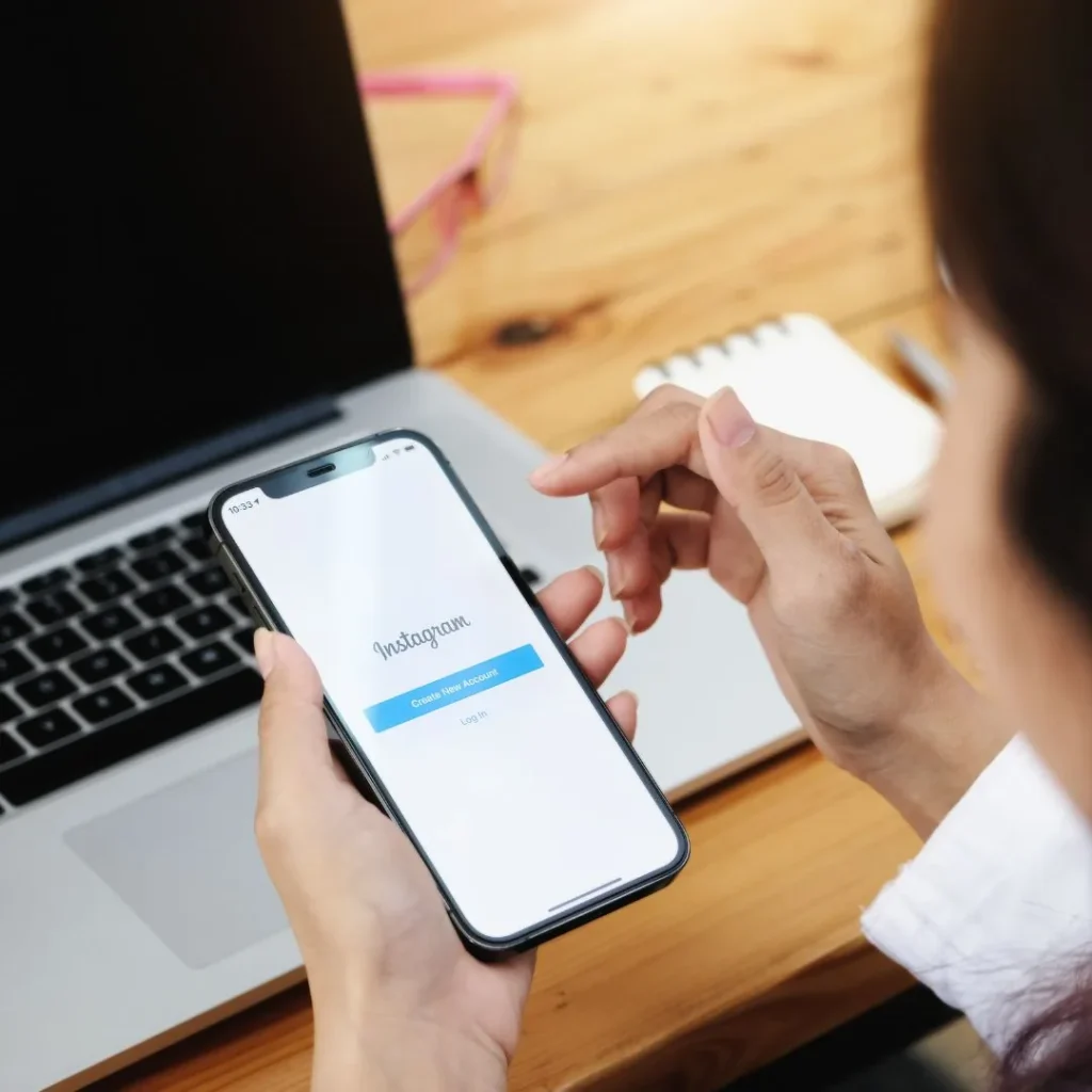 Mujer con un móvil que muestra la pantalla de inicio de sesión de Instagram frente a un portátil