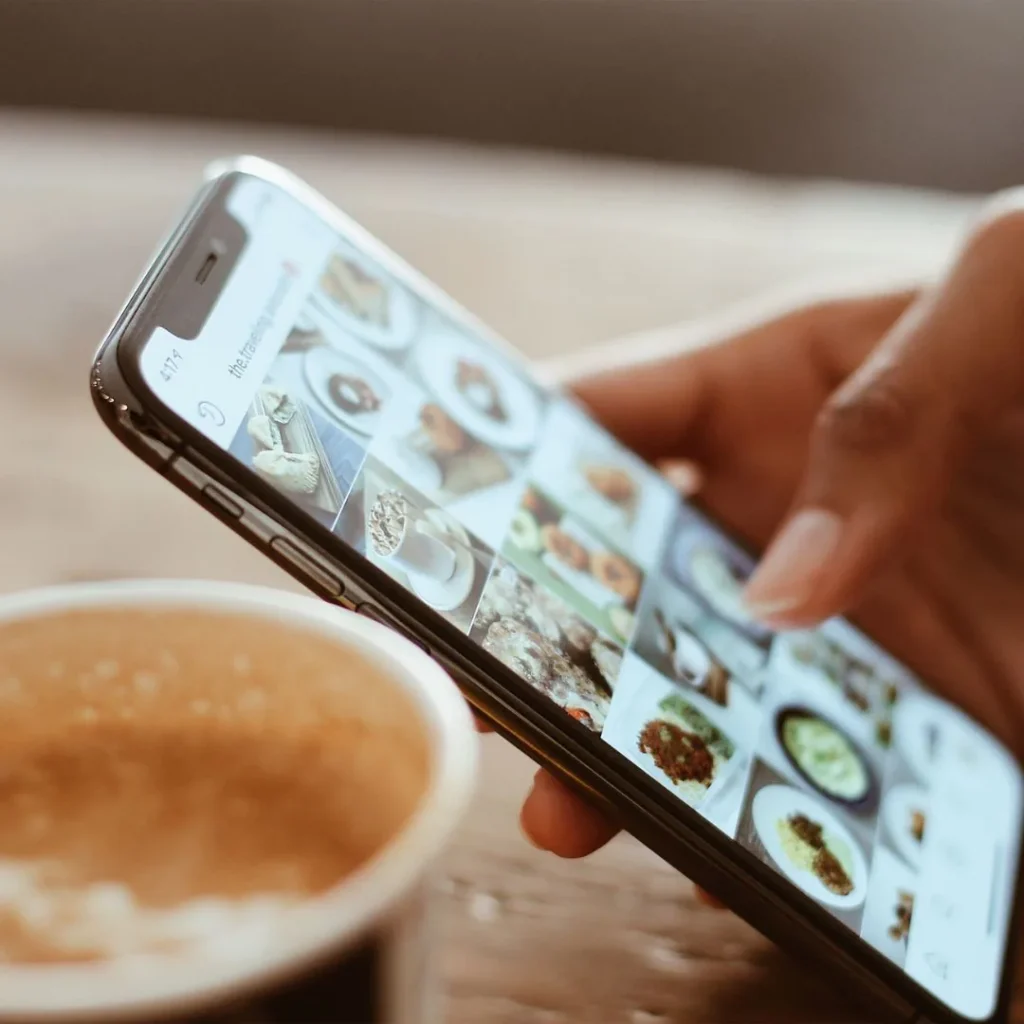 Main faisant défiler un fil de photos culinaires sur un smartphone à côté d'un café