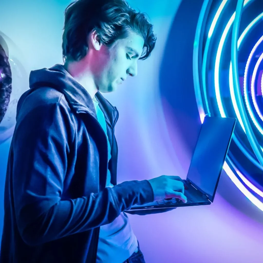 Jeune homme utilisant un ordinateur portable devant une installation lumineuse au néon