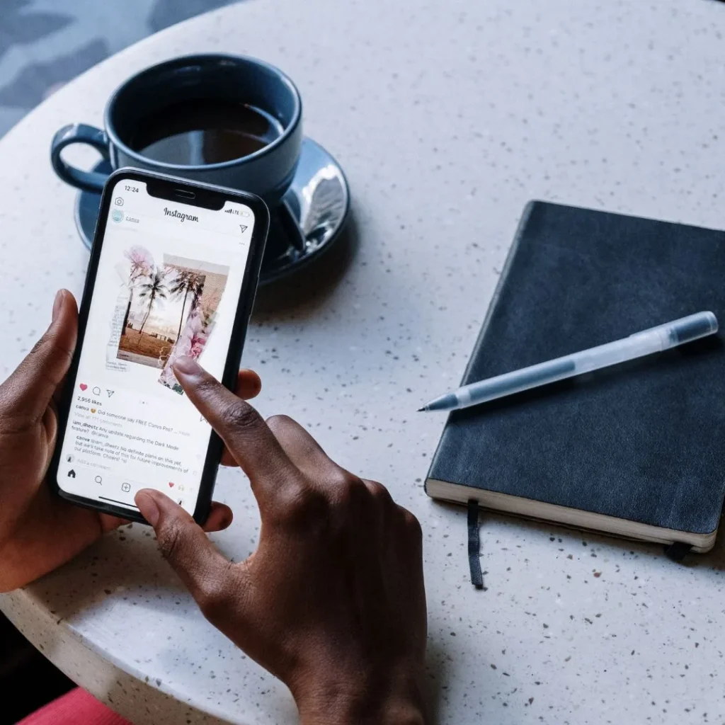 Manos deslizando por Instagram en un móvil junto a una taza de café y una libreta