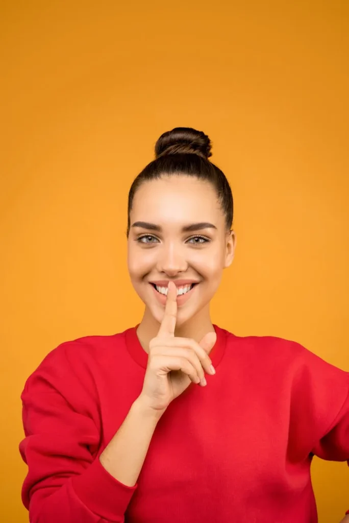 Mujer con jersey rojo pidiendo silencio con el dedo en los labios