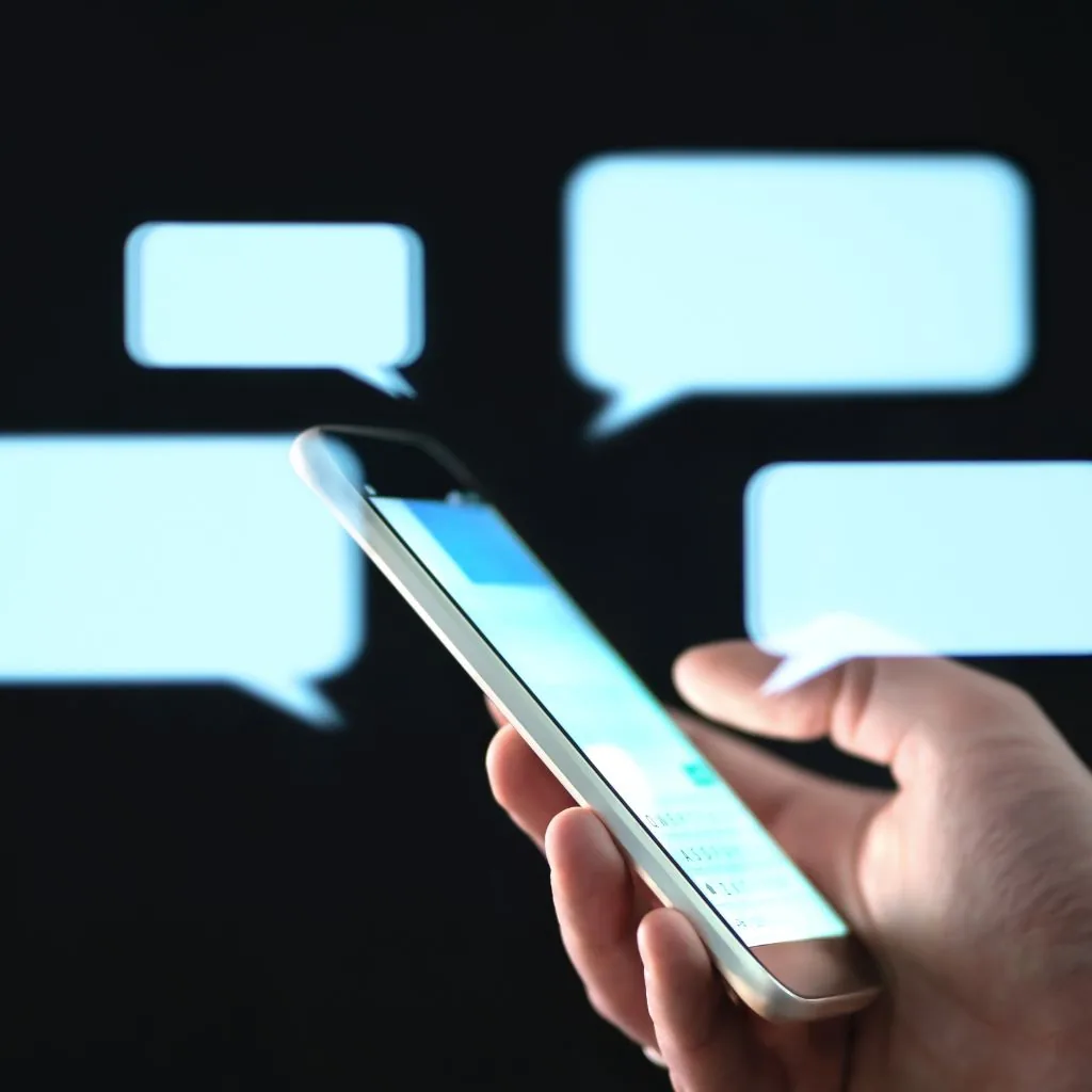 Hand met een smartphone omringd door oplichtende chatballonnen