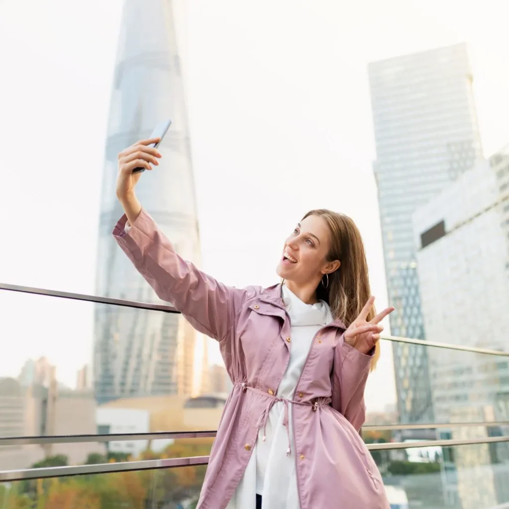 Mujer sonriente haciéndose un selfi frente a rascacielos