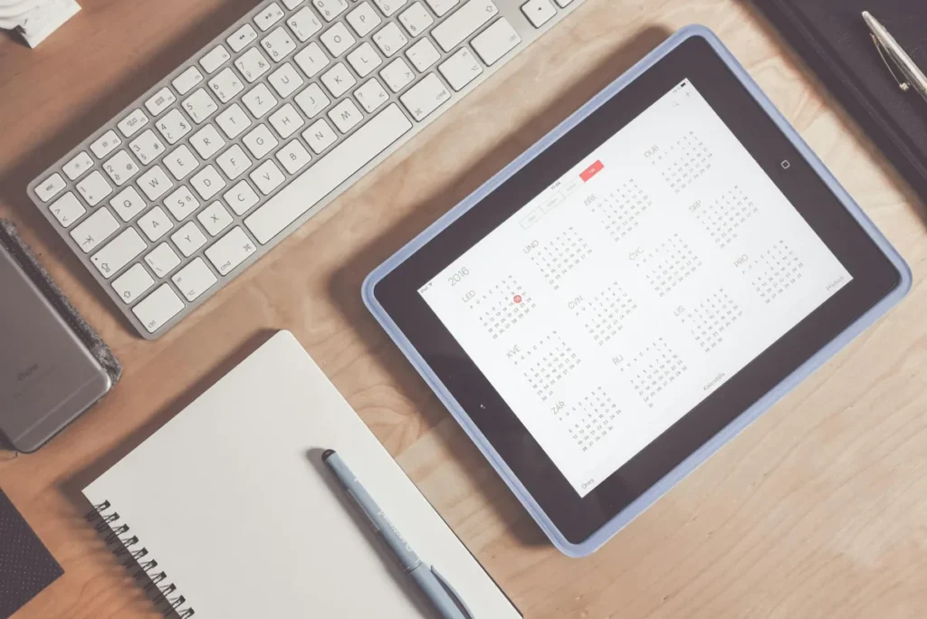 iPad con un calendario junto a un teclado y una libreta
