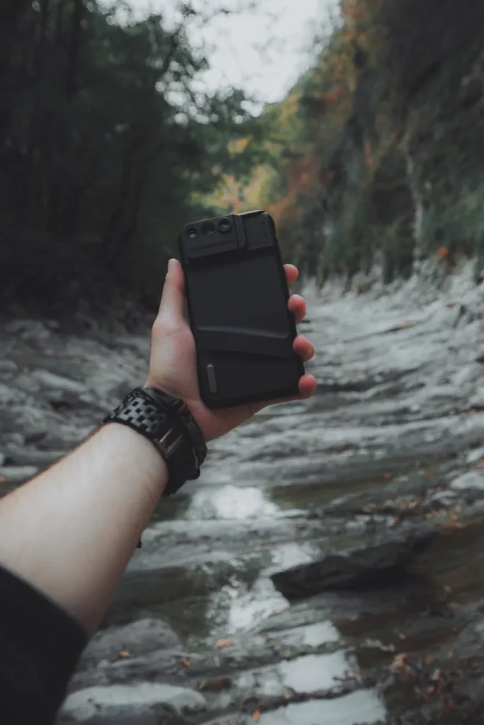 Mano sosteniendo un móvil para fotografiar un río en el bosque