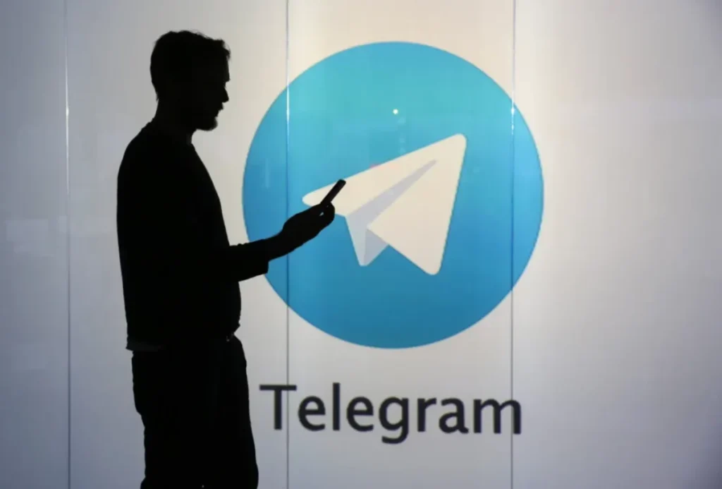Silhouette of a man on his phone in front of the Telegram logo